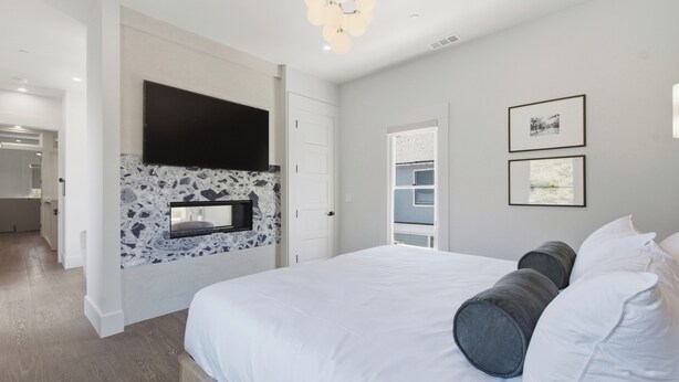 Un dormitorio con una cama, un televisor montado y dos cuadros en la pared.