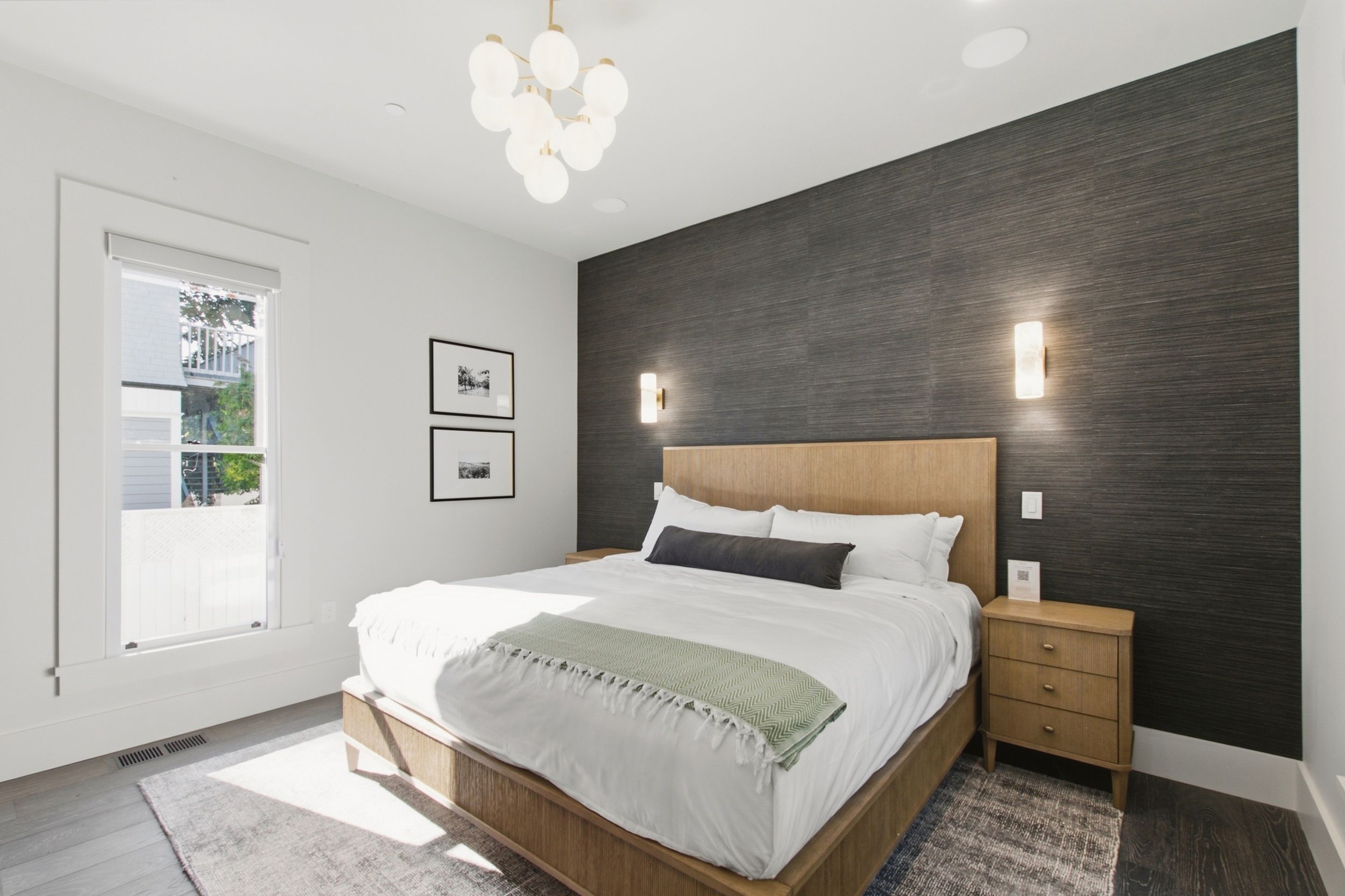 A modern bedroom with a large bed, bedside tables, a dark accent wall, and a window with a view.