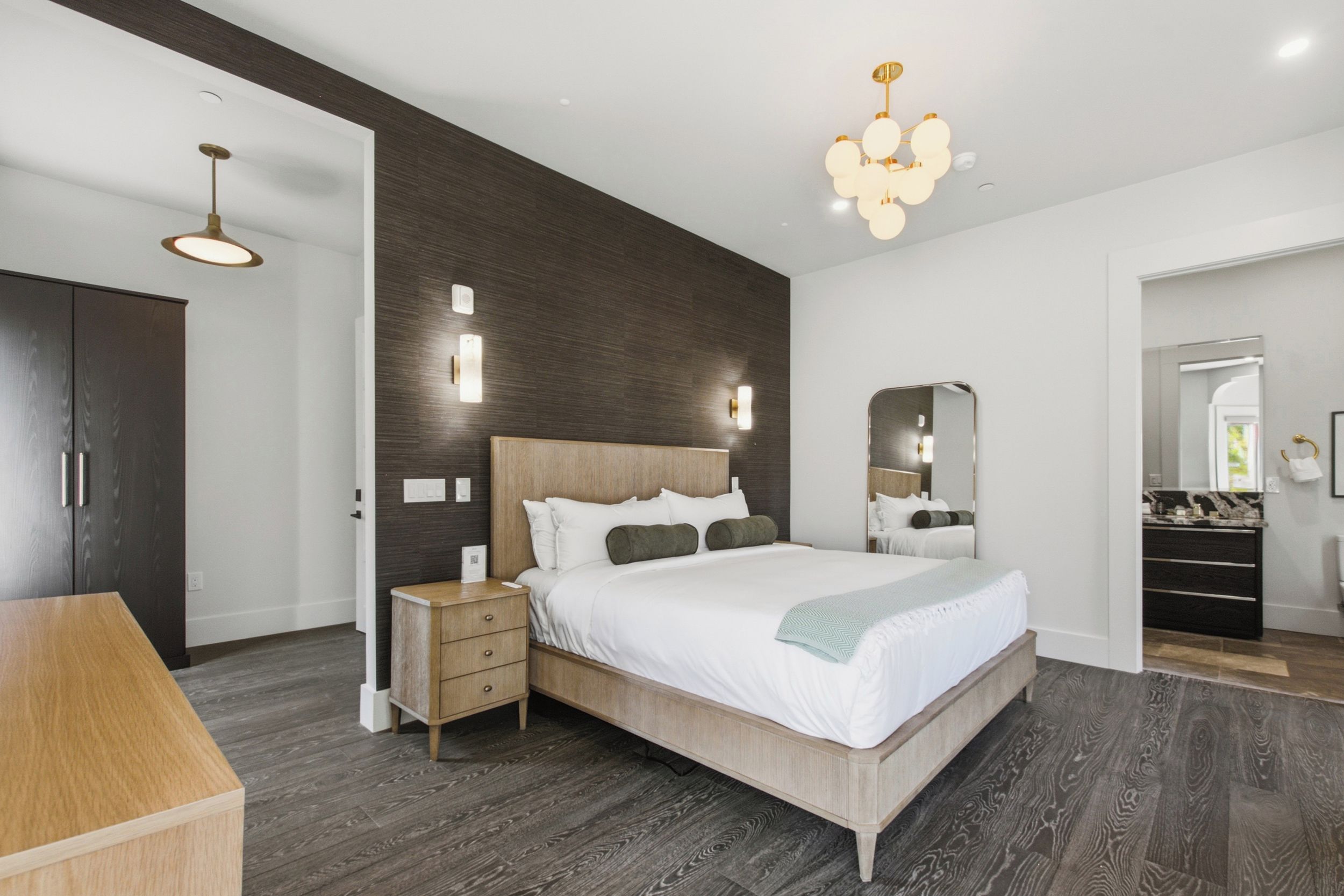 A modern bedroom with a large bed, bedside tables, a wardrobe, and a bathroom visible through an open door.