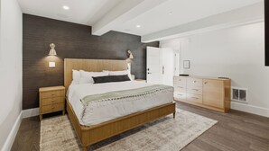 A modern bedroom with a wooden bed, bedside lamps, a wardrobe, and a large mirror.
