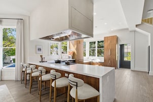 A modern kitchen with a central island, bar stools, and large windows.