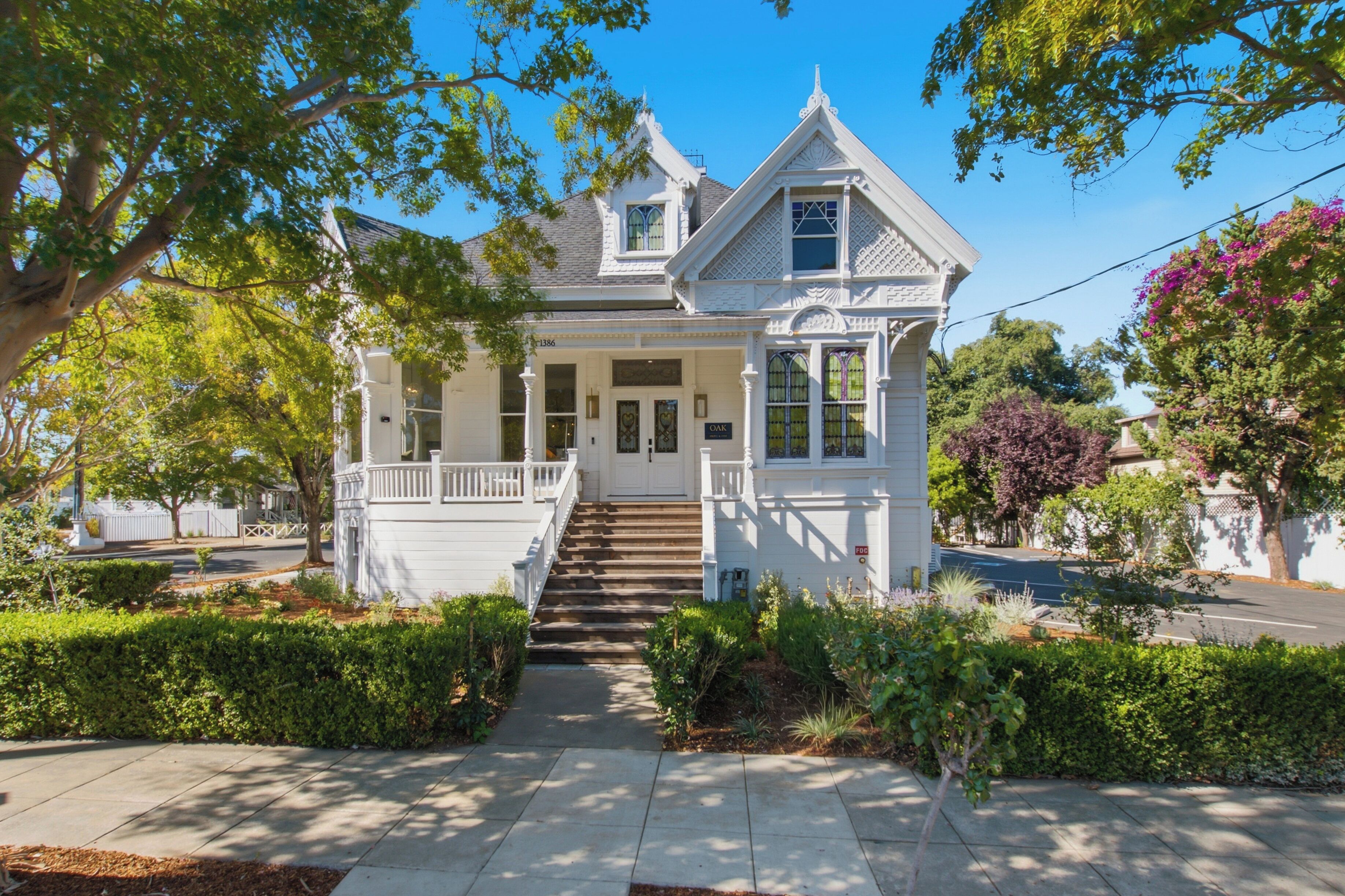 A two-story white house with a front porch, a staircase leading to the entrance, and a well-maintained garden.