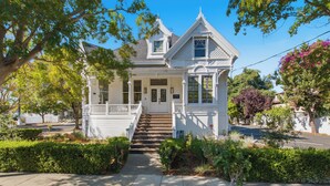 A two-story white house with a front porch, a staircase leading to the entrance, and a well-maintained garden.