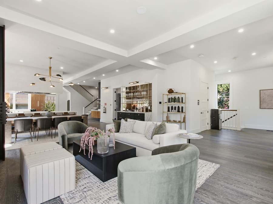 A spacious living area with a modern design, featuring a white sofa, a coffee table, and a dining area with a kitchen in the background.