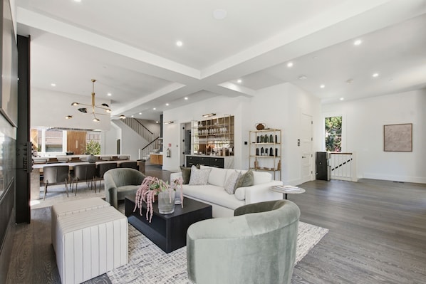 A spacious living area with a modern design, featuring a white sofa, a coffee table, and a dining area with a kitchen in the background.