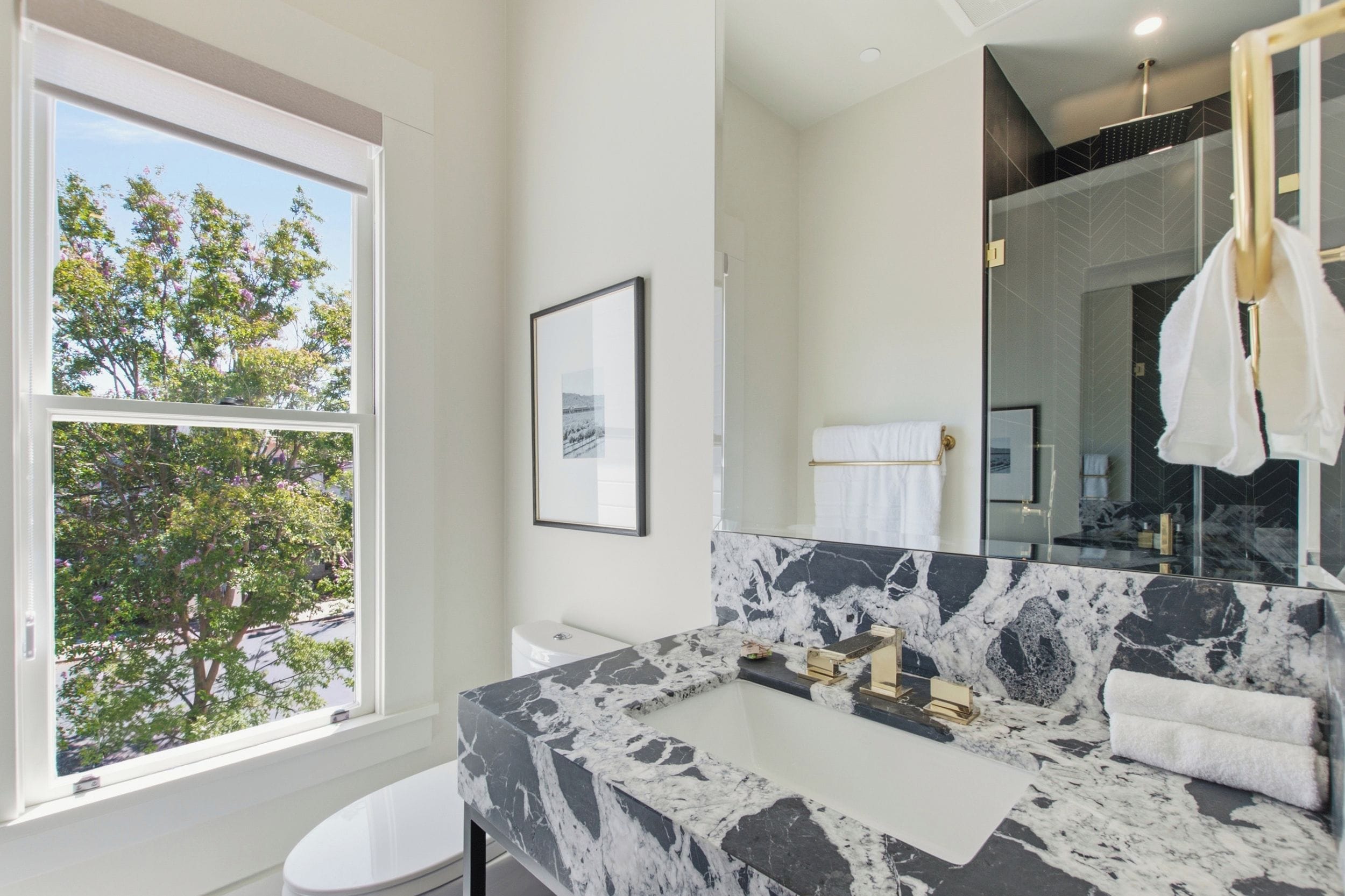 A bathroom with a large window, a marble sink, and a toilet.