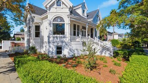 A large, white, two-story house with a prominent front porch and a staircase leading to the entrance.