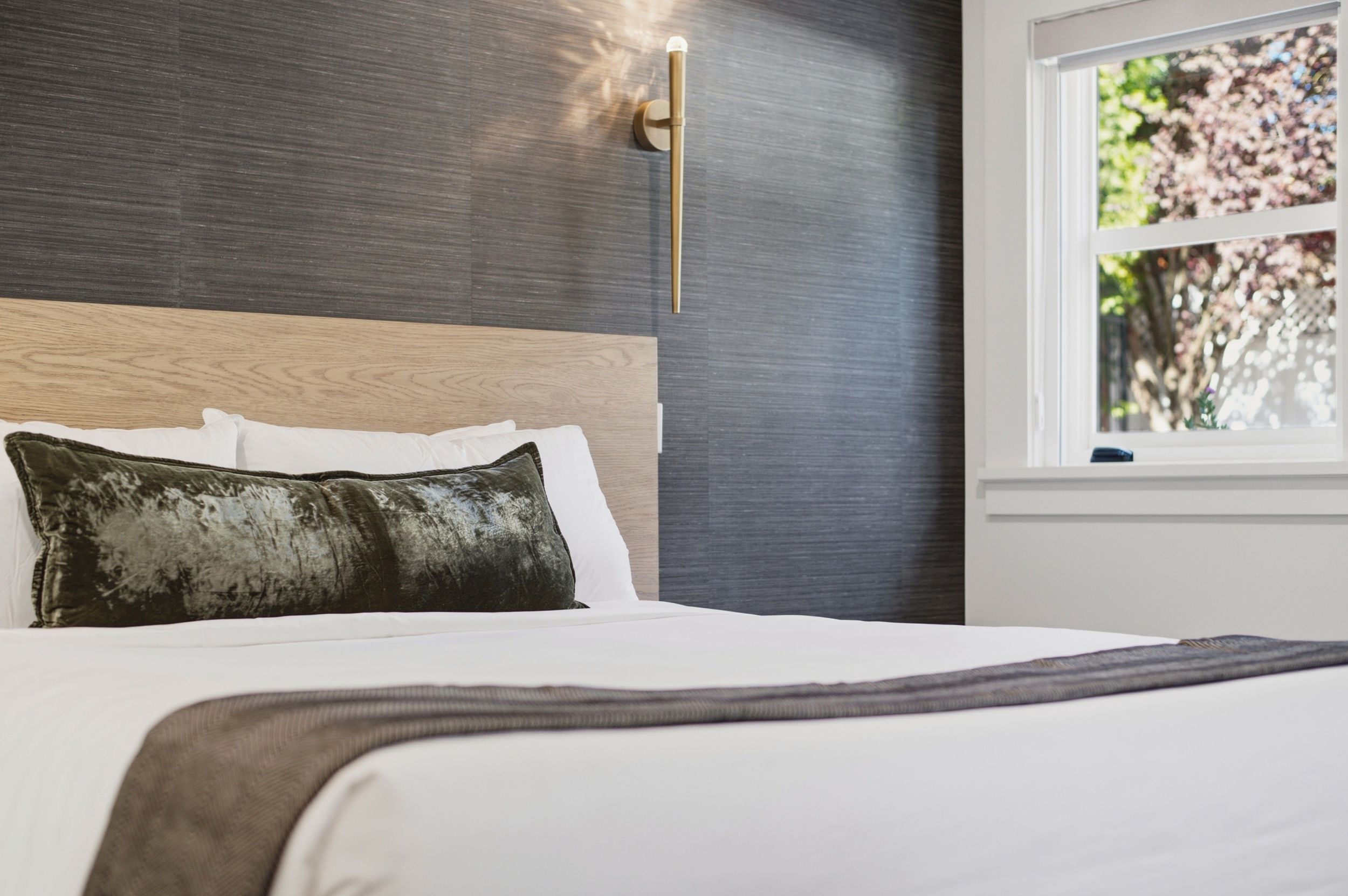 Ein Bett mit einem hölzernen Kopfteil, einem dunkelgrünen Kissen und einer weißen Decke.