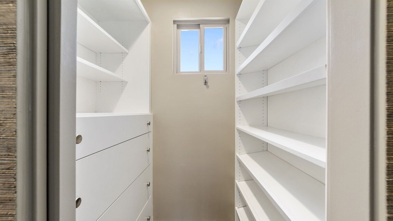Un vestidor estrecho con estantes abiertos y una puerta con ventanal.