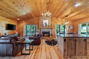 A wooden cabin interior with a fireplace, leather furniture, and a stone wall. - Hiker’s Hideaway | Hot Tub • Games • Dog Friendly (Suches)
