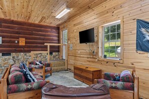 A log cabin interior with a stone wall, a television mounted on the wall, and a flag. - Hiker’s Hideaway | Hot Tub • Games • Dog Friendly (Suches)