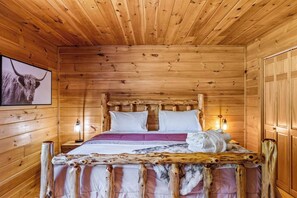 Quarto de cabana de madeira com uma cama, uma imagem de animal pendurada e uma mesa de cabeceira com luminária.