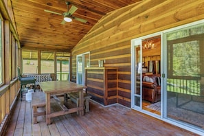 A wooden cabin with a dining area, a ceiling fan, and a sliding glass door leading to a living room with a couch. - Hiker’s Hideaway | Hot Tub • Games • Dog Friendly (Suches)