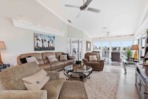 A spacious living room with a brown leather sofa, a glass coffee table, and a view through large windows. - Come relax for a stay on Gorgeous Perico Bay Island. (Bradenton)