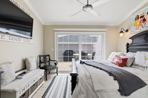 Ein Schlafzimmer mit einem Bett, einem an der Wand befestigten Fernseher, einem Deckenventilator und Blick ins Freie durch eine Schiebetür.