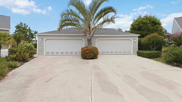 Garagem residencial com palmeira e arbusto de flores na entrada.
