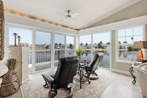 Une véranda avec de grandes fenêtres, un ventilateur de plafond et deux fauteuils en cuir.
