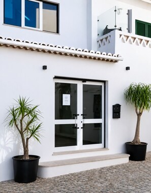 A building with a white facade, a glass door entrance, and two potted plants. - Spacious Beach Flat · 5-Min Walk to Beach & Restaurants (Luz)
