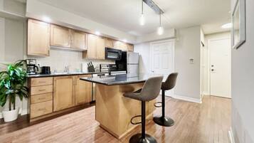 A modern kitchen with wooden cabinets, a central island with bar stools, a microwave, and a coffee maker.