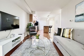 Ein modernes Wohnzimmer mit einem Flachbildfernseher, einem grauen Sofa, einem Couchtisch und einem Essbereich im Hintergrund.