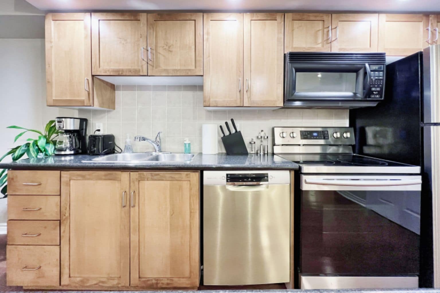 A kitchen with wooden cabinets, a stainless steel dishwasher, a microwave, an oven, and a sink.