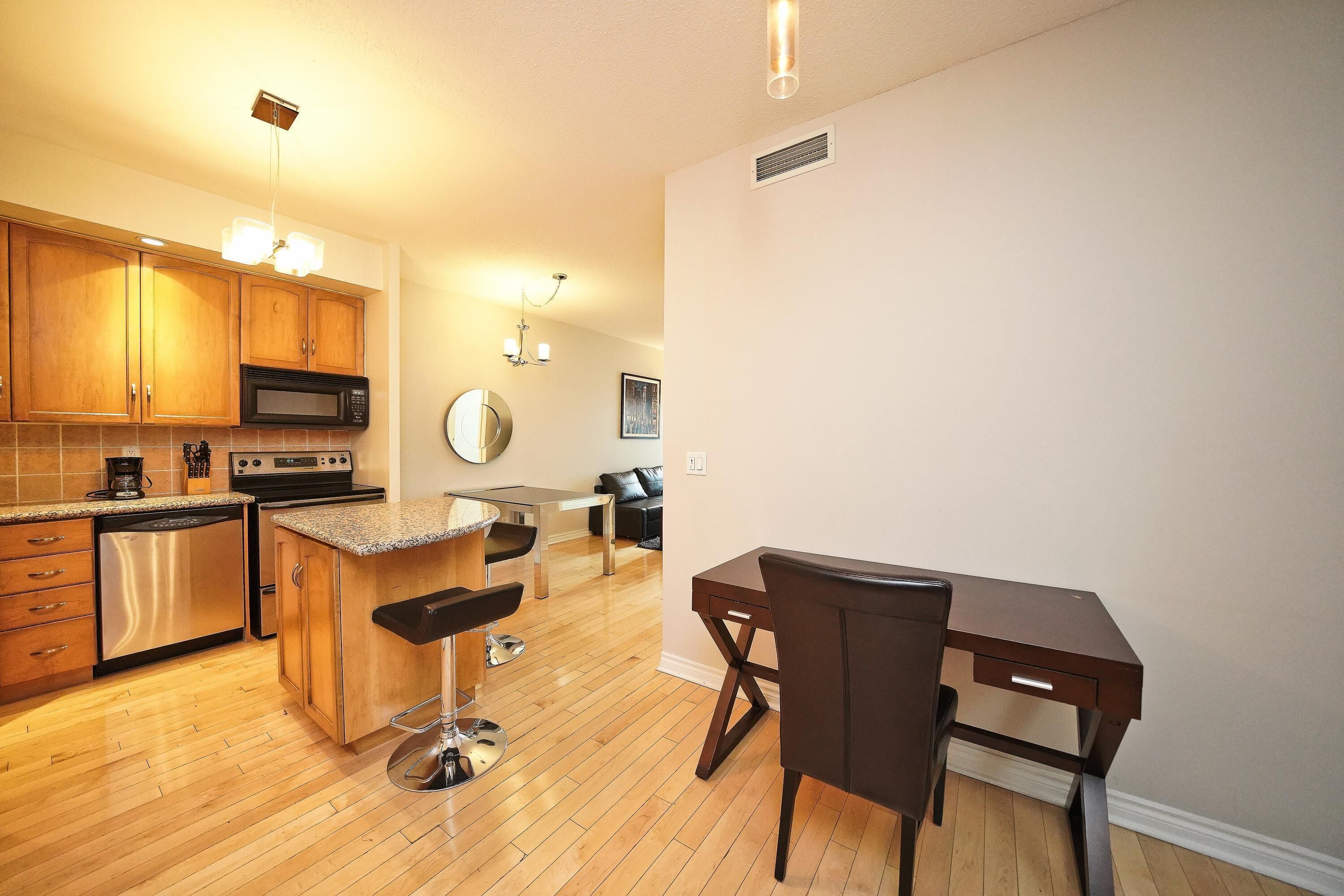 A modern kitchen with wooden cabinets, stainless steel appliances, a bar area, and a dining table with chairs.