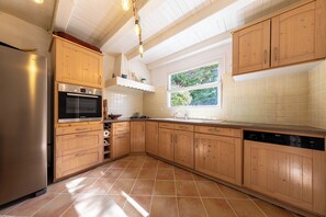 A kitchen with wooden cabinets, a Bosch oven, and a window with a view of greenery. - Villa l'Écrin Beige - Les Portes en Ré (Les Portes-en-Ré)