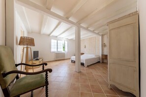 Una habitación con una cama, una silla, un televisor sobre un mueble de madera y un radiador.