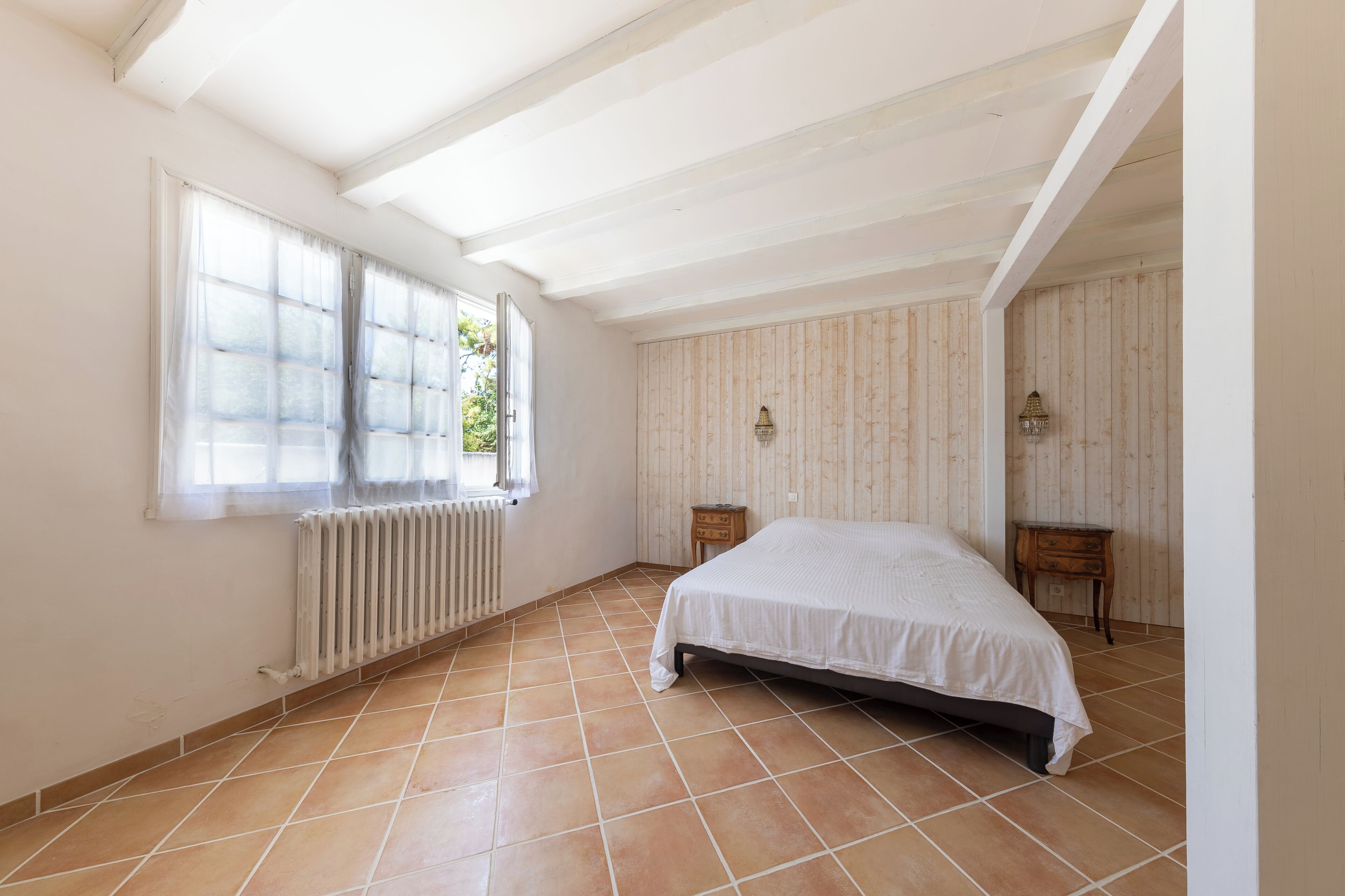 A bedroom with a bed, a radiator, a window with curtains, and a wooden wall.