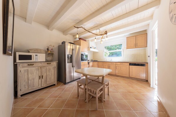 Una cocina con una mesa de madera, armarios, un refrigerador y una ventana.