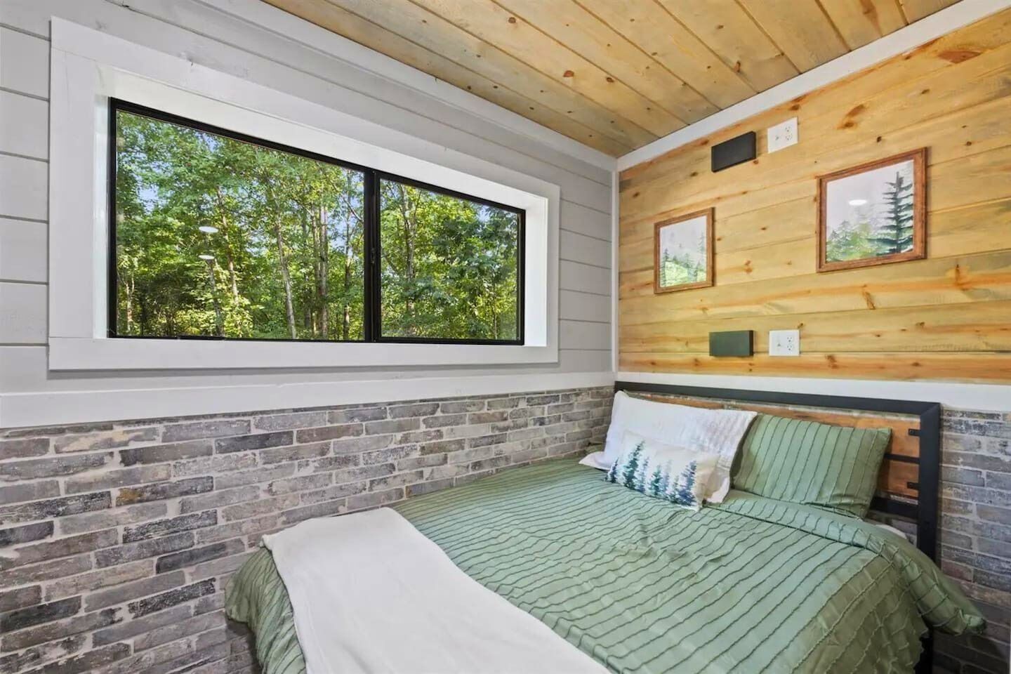 A bedroom with a large window, a brick wall, and a wooden ceiling.