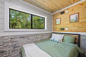 A bedroom with a large window, a brick wall, and a wooden ceiling. - NEW! Lux, Hot Tub, Game Room, King Suites, Lounge (Broken Bow)