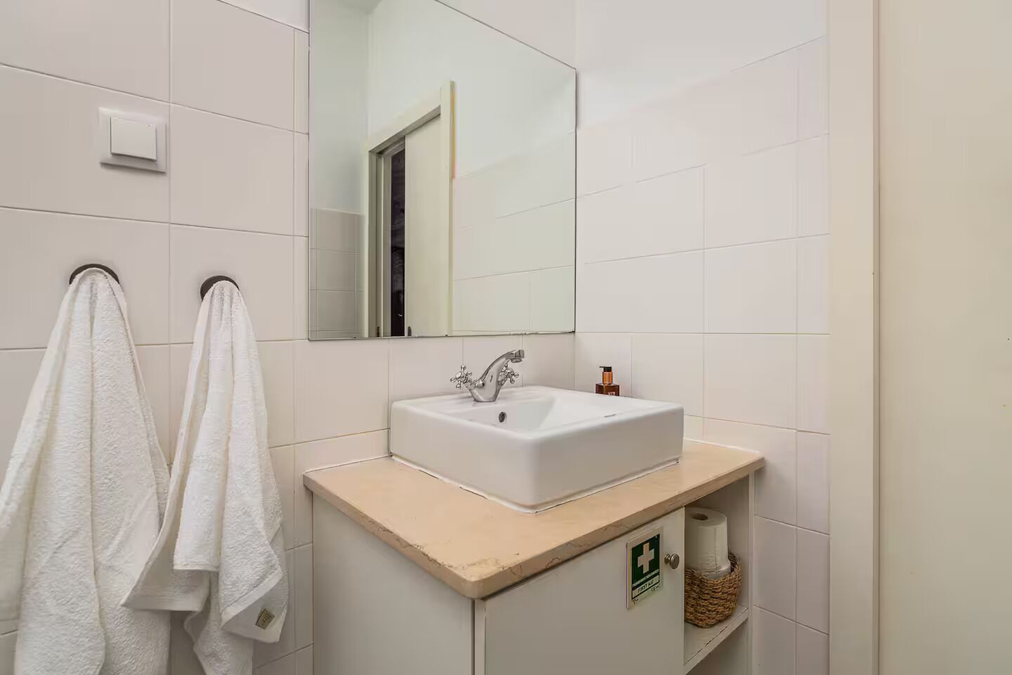 Une salle de bain avec un lavabo blanc, un miroir et deux serviettes suspendues à un porte-serviettes.