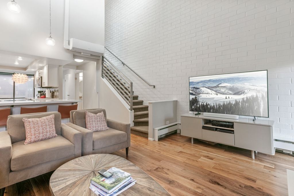 A modern living room with a sofa, coffee table, and a flat-screen TV against a white brick wall.