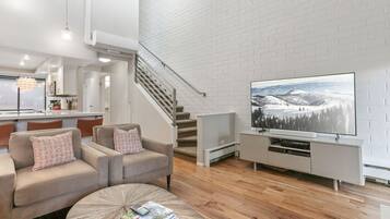 A modern living room with a sofa, coffee table, and a flat-screen TV against a white brick wall.