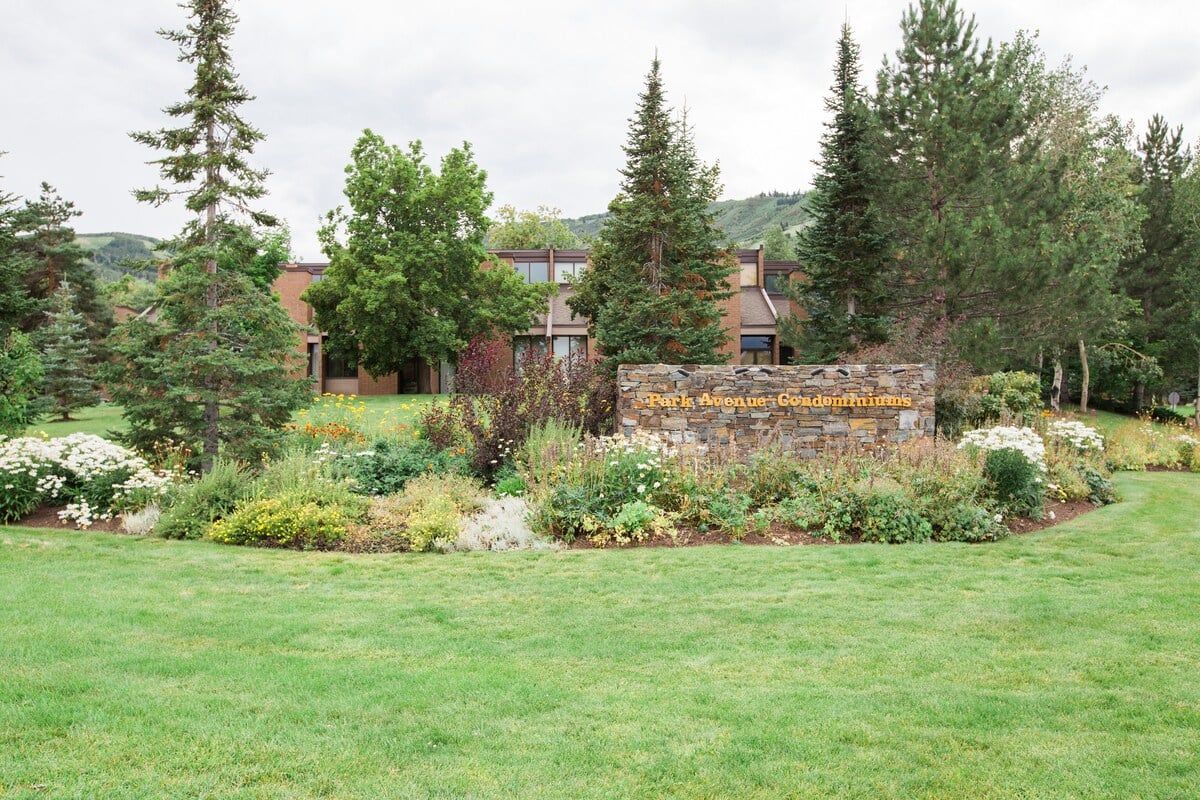 A building with a stone sign in front, surrounded by a well-maintained lawn and various trees.