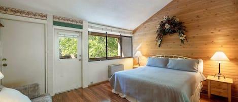 Un dormitorio con cama, lámparas de noche, un muro de madera, una puerta y una ventana.