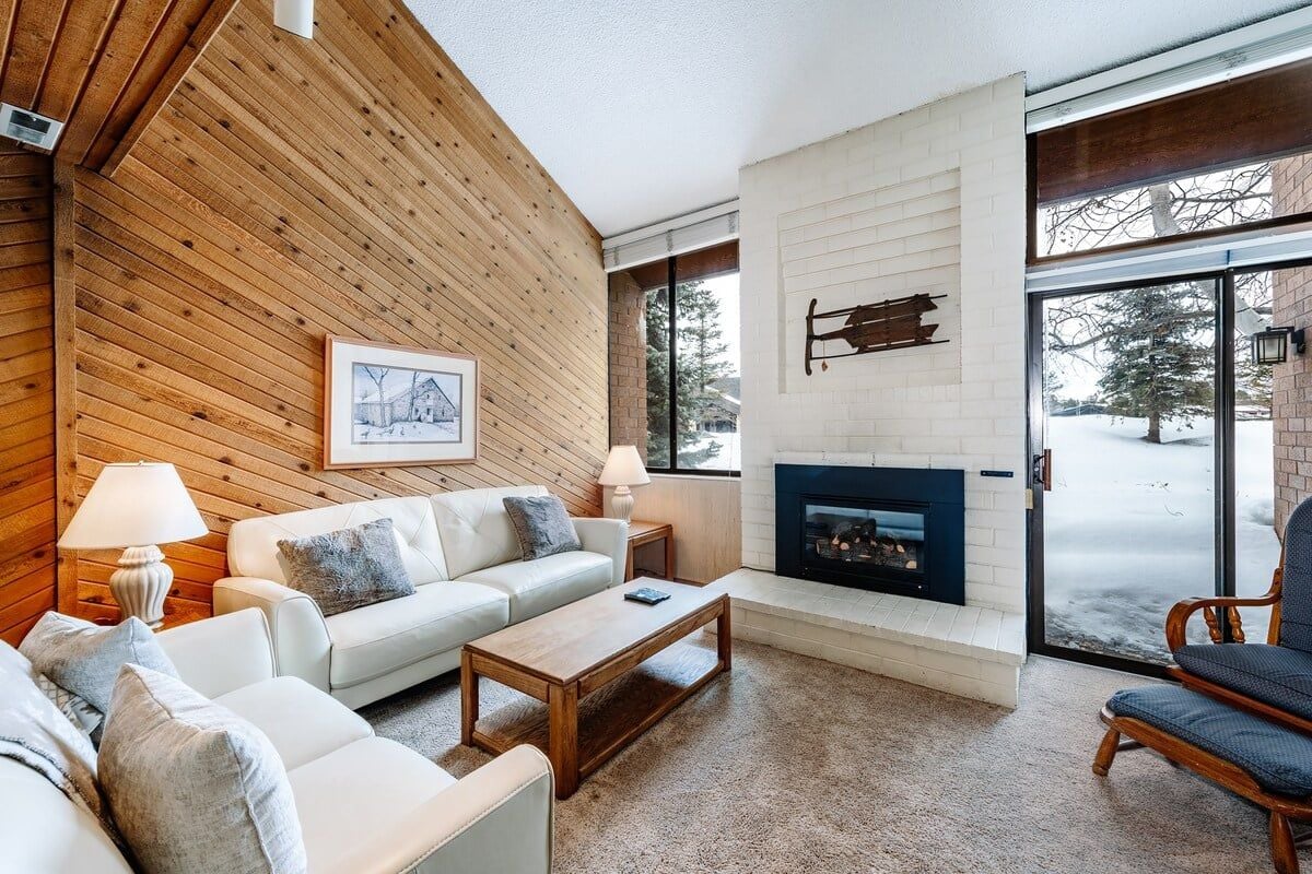 A modern living room with a fireplace, wooden walls, and a large window.