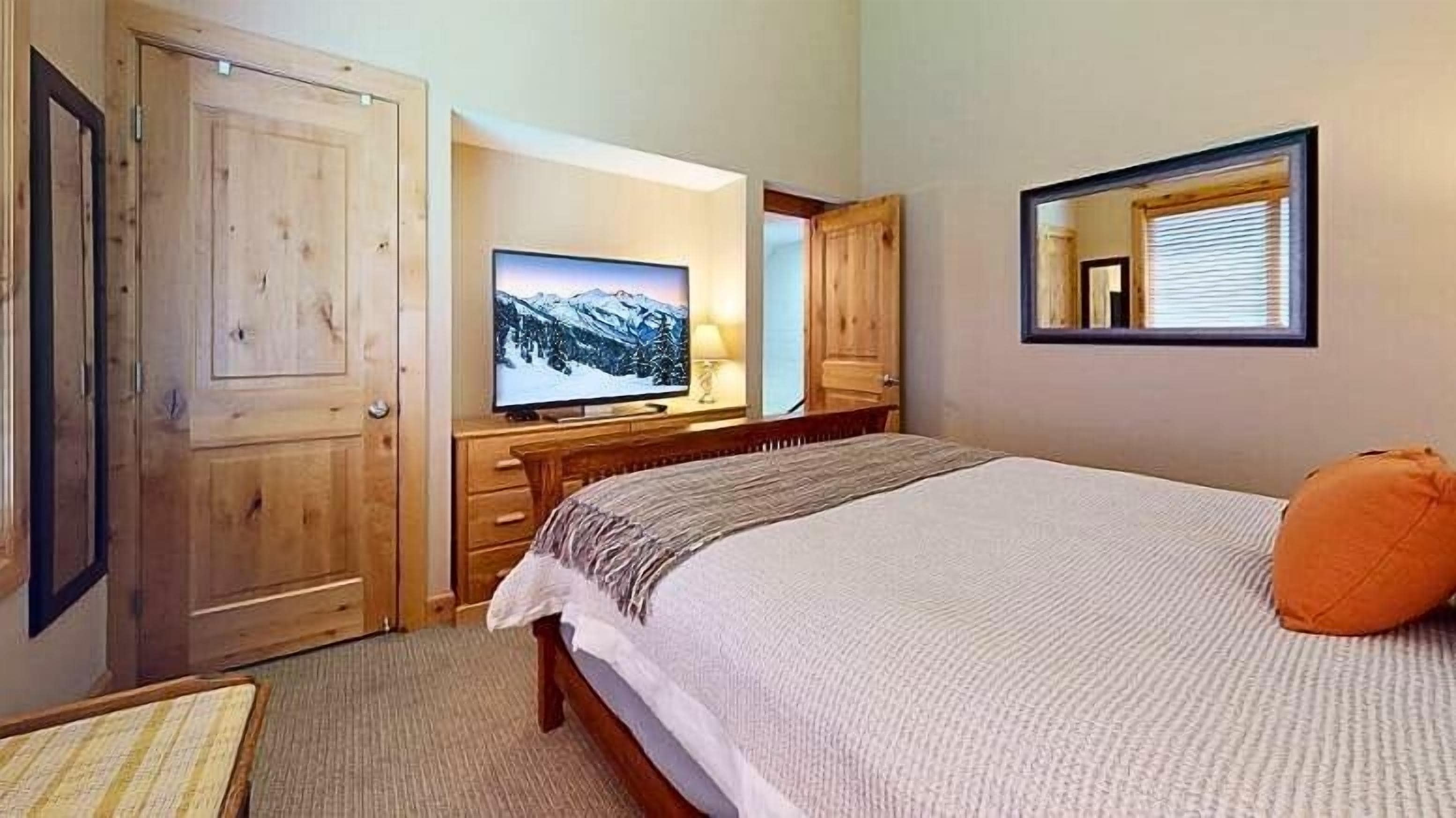 A bedroom with a bed, a television, a wooden wardrobe, and a mirror.