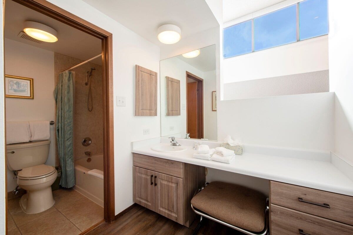 A bathroom with a toilet, shower, sink, and mirror.