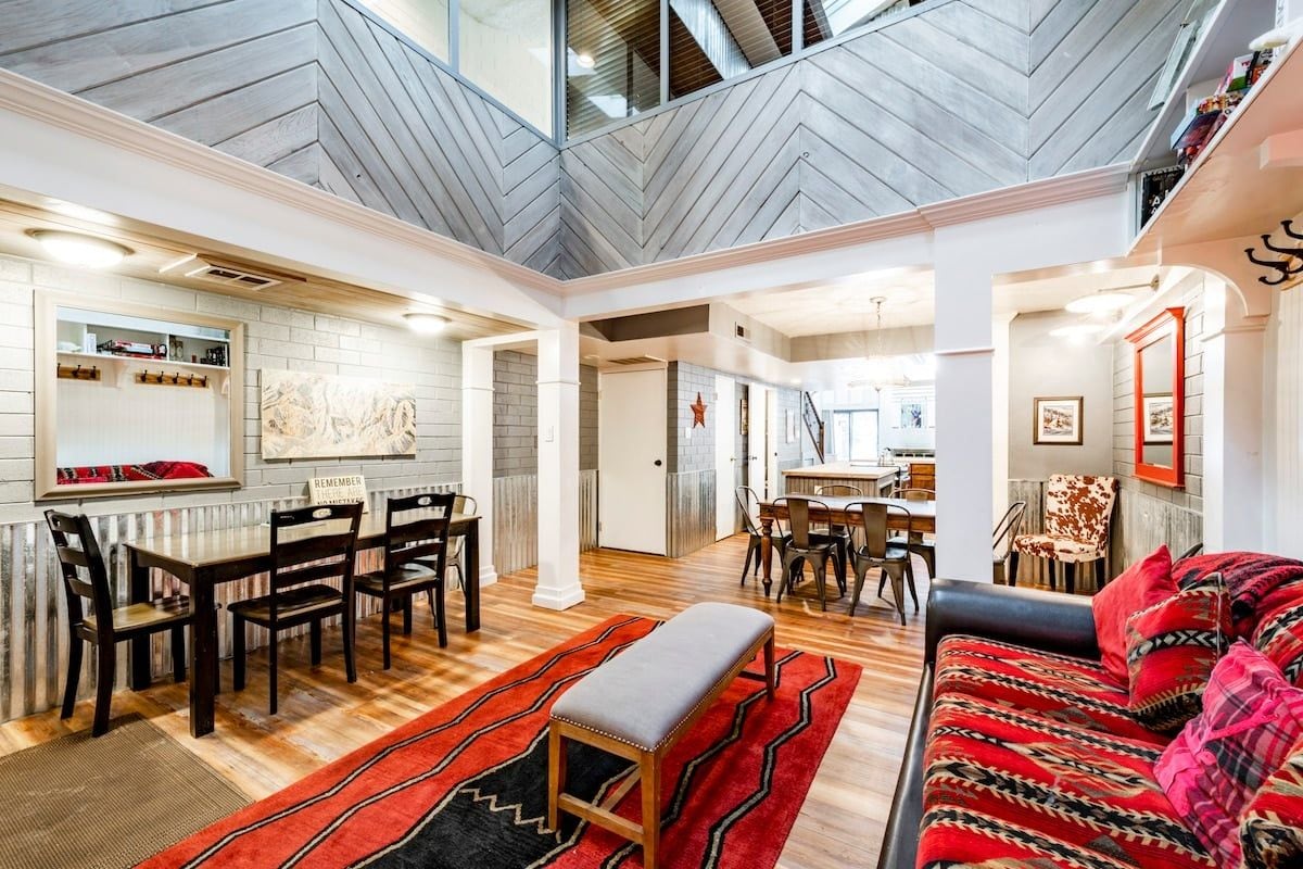 A spacious living area with a high ceiling, a dining area, and a kitchen in the background.