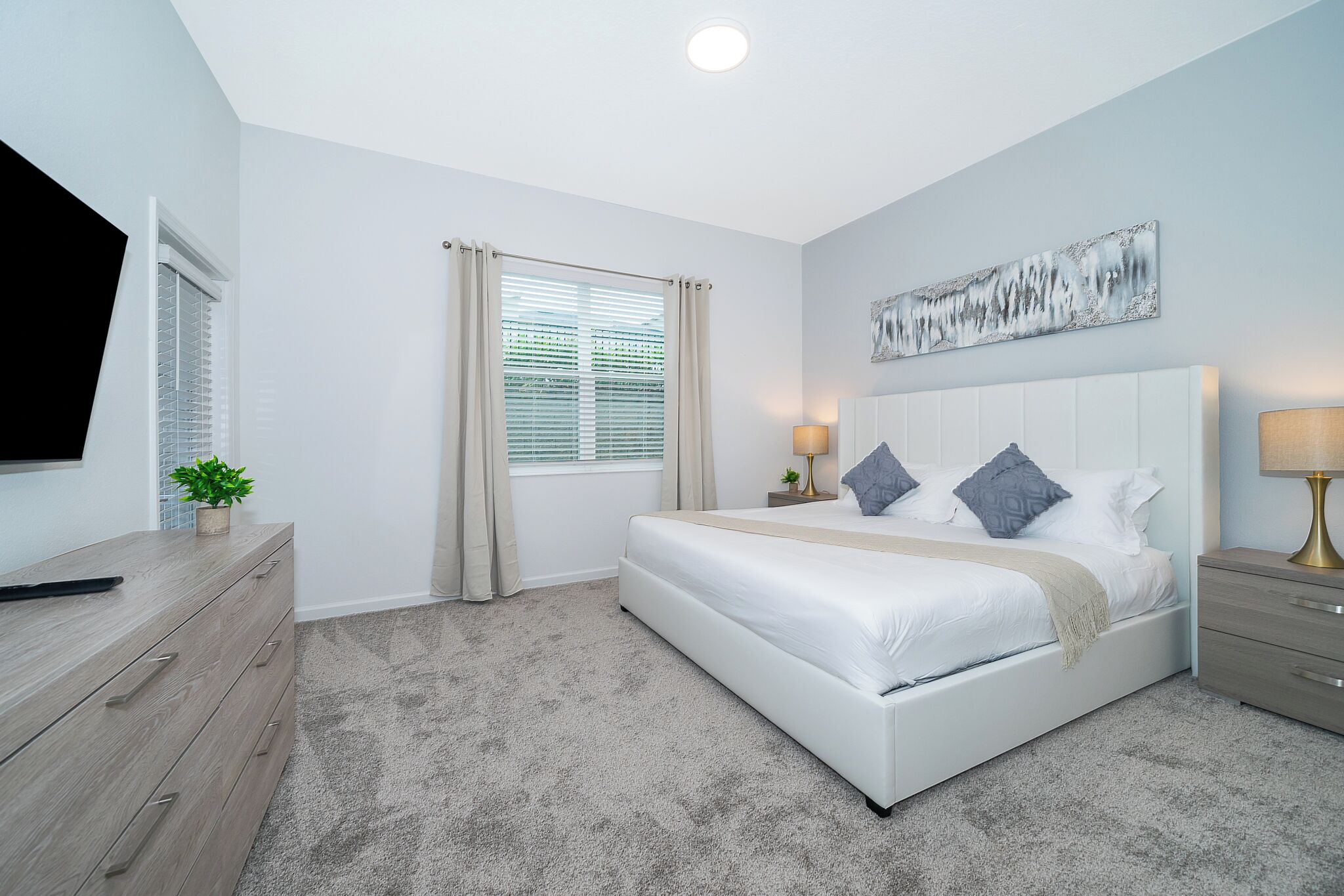 A bedroom with a bed, bedside tables, a TV, and a window with curtains.