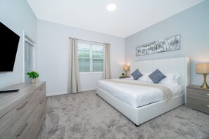 Un dormitorio con cama, mesitas de noche, televisión y ventana con cortinas.