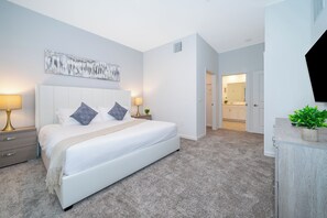 Een moderne slaapkamer met een groot bed, nachtlampjes, een schilderij aan de muur en uitzicht op de badkamer.