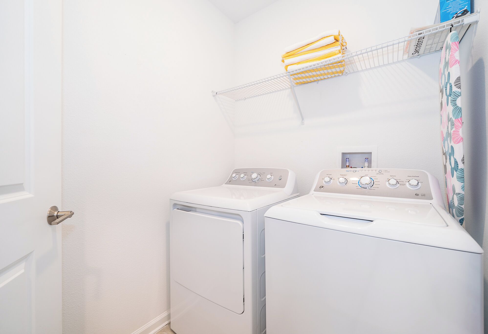 A laundry room with two white front-loading washing machines and a metal shelf above them.