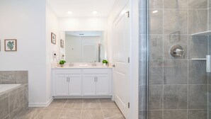 Une salle de bain moderne avec une douche à l’italienne en verre, des meubles blancs et un grand miroir au-dessus du lavabo.