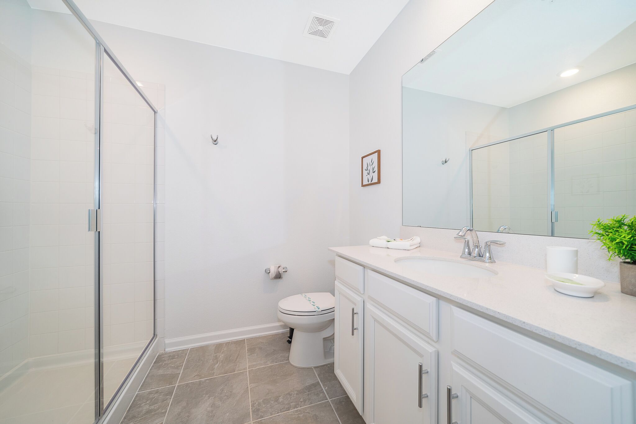A modern bathroom with a glass shower enclosure, a toilet, a sink with a mirror, and a potted plant.