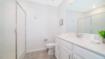 A modern bathroom with a glass shower enclosure, a toilet, a sink with a mirror, and a potted plant.