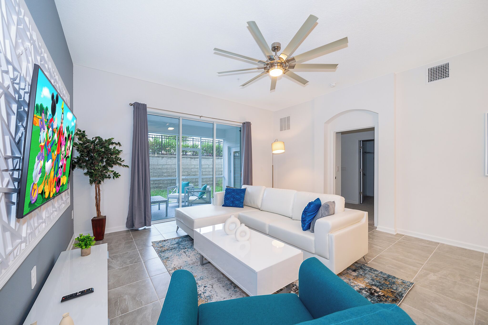A modern living room with a white sofa, blue armchairs, a flat-screen TV, and a ceiling fan.