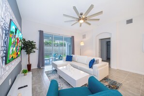 Una sala de estar moderna con un sofá blanco, sillones azules, un televisor de pantalla plana y un ventilador de techo.